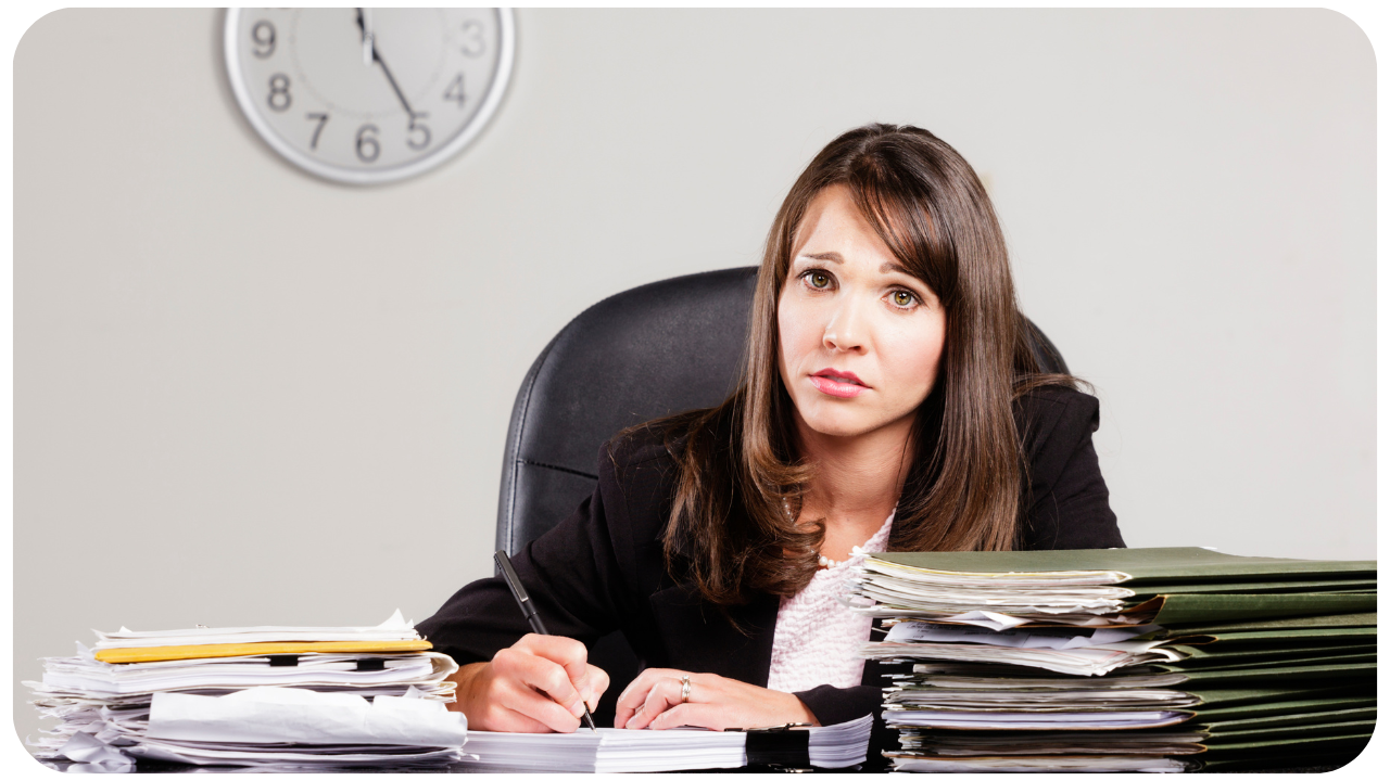 woman sitting at her office desk with papers stacked high feeling burnt out