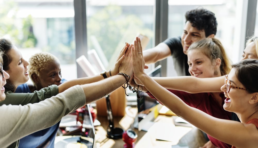 Smiling coworkers in an office join hands in a group high-five, celebrating teamwork and success